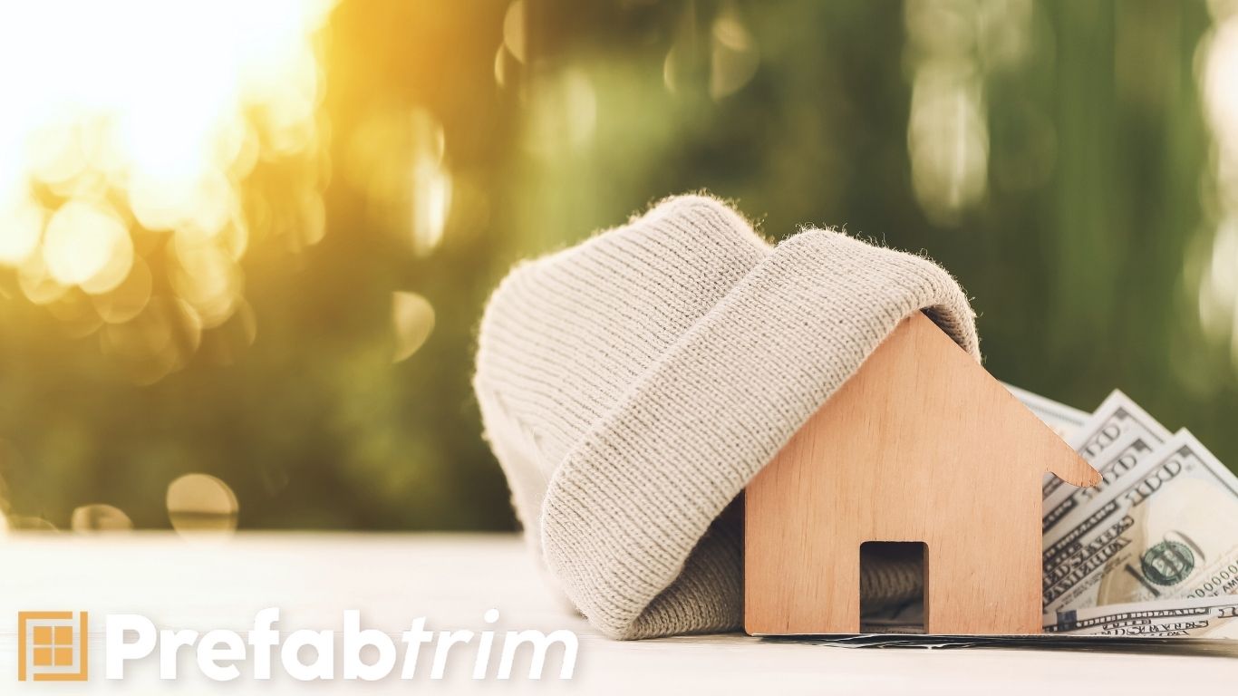 Energy-Efficient Window Trim to Prevent Drafts and Save Money | PrefabTrim Wooden house wrapped in a cozy knit hat with dollar bills underneath, symbolizing energy-efficient window trim that prevents window drafts and saves on heating costs.